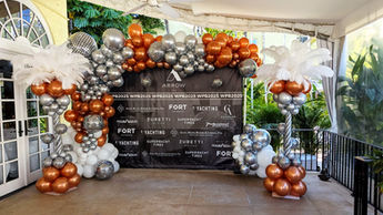 Disco themed backdrop decorated with custom printed backdrop, silver and copper balloon arch with disco balls, and elegant columns of balloons with white ostrich feathers