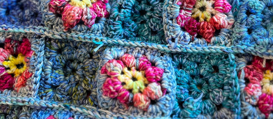 Crocheted blanket with blue squares and colorful floral patterns. Lively colors create a vibrant, textured visual on a wooden surface.