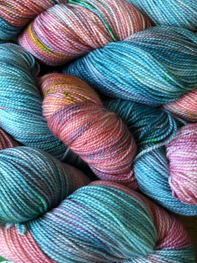 Close-up of colorful yarn skeins in pink, blue, and green tones. The textures and vibrant patterns create a cozy, artistic feel.