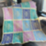 Crocheted blanket with butterfly patterns in teal, blue, purple, and pink, draped over a sofa. Sunlight filters through a nearby window.