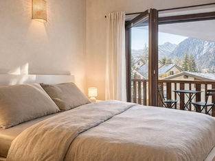Letto matrimoniale accogliente con biancheria in lino neutro e balcone panoramico sulle montagne, esempio di valorizzazione immobiliare e home staging professionale.