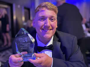 Senior Customer Hub Agent Laurence Bowden smiling, holding CSA Award Trophy for Merit Award 2025