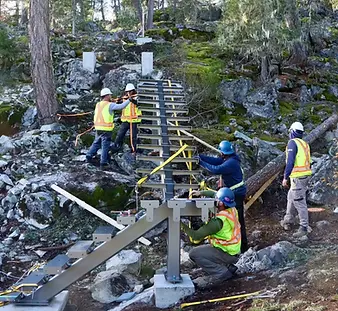 Crew assembling a custom steel stair system on a steep wooded hillside