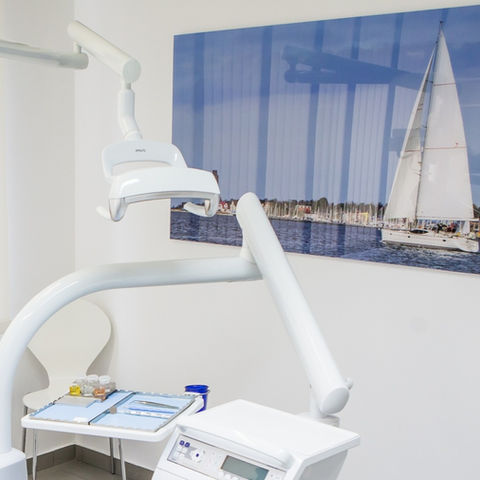Behandlungszimmer eines Zahnarztes mit einem großen Bild mit einem Segelboot darauf an der Wand