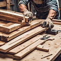 Carpentry workshop with stacked wood panels, cutting tools, workbench, and a worker measur