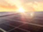 Paneles solares bajo un cielo anaranjado al atardecer, con un intenso resplandor del sol.