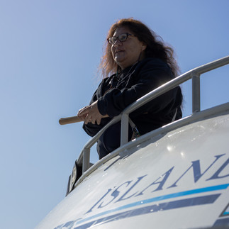 A Chumash woman holding  traditional clapping sticks is seen leaning on the railing of a boat