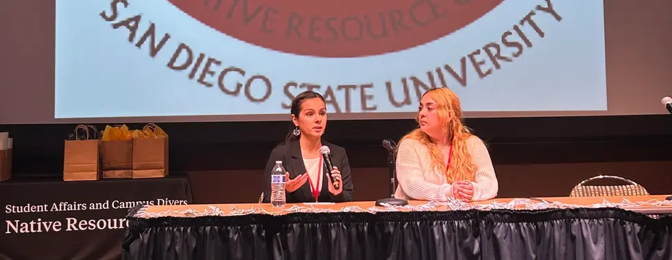 A panel of two people sit behind a table on a stage