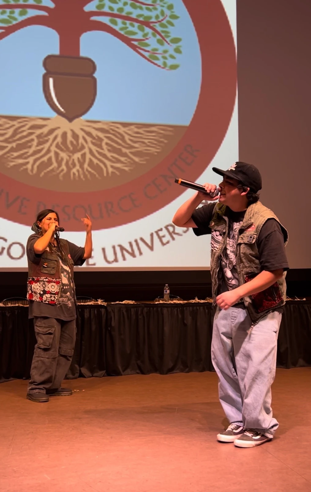 Two people sing into microphones on a stage