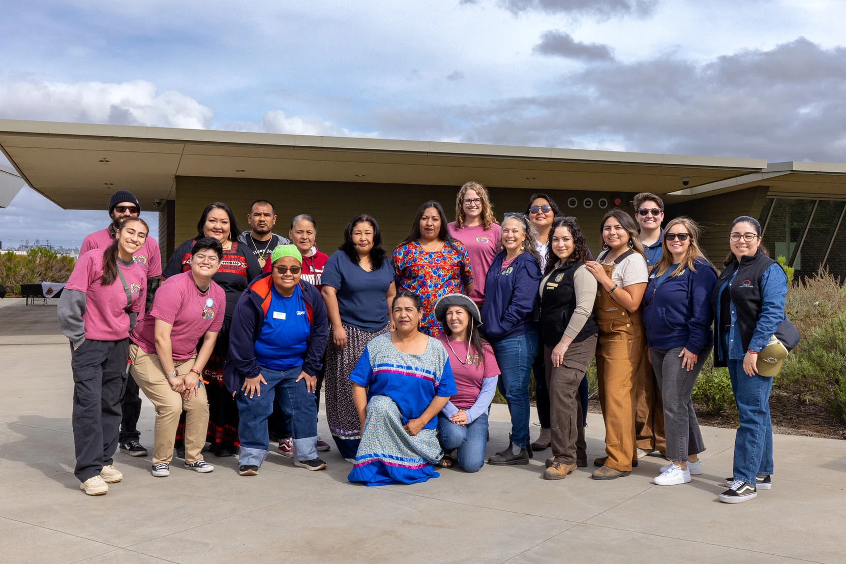 A group of people stand smiling together outside in front of a building