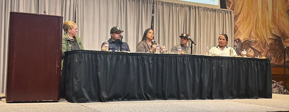 A panel of five people sit behind a table on a stage.