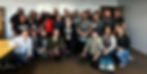 A group of people smile together inside a classroom.