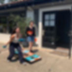 Amira and Solana play Climate Kids corn toss outside on a sunny day, with Amira mid-throw and Solana watching.