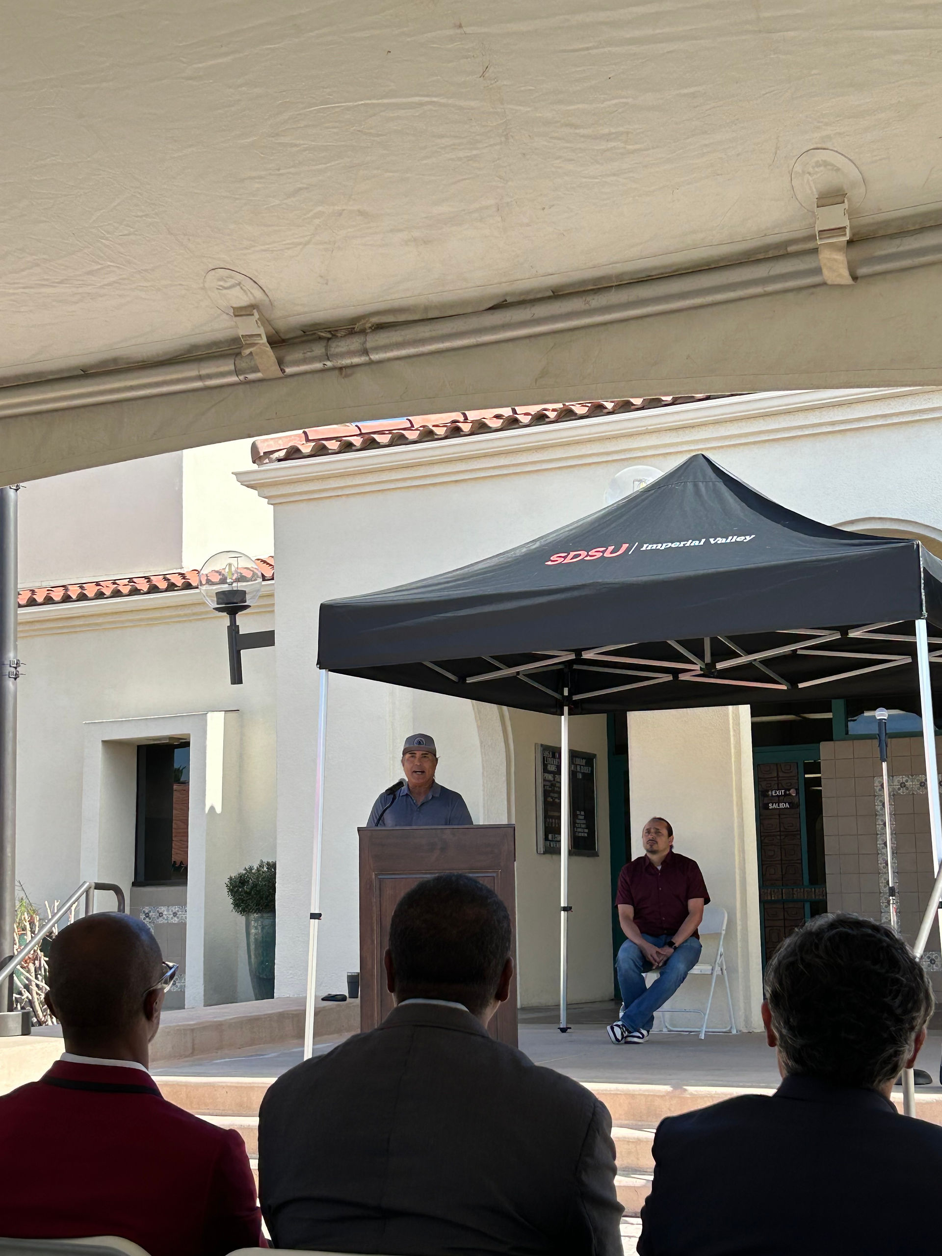 A person stands at a podium addressing a crowd who is seated in front of them