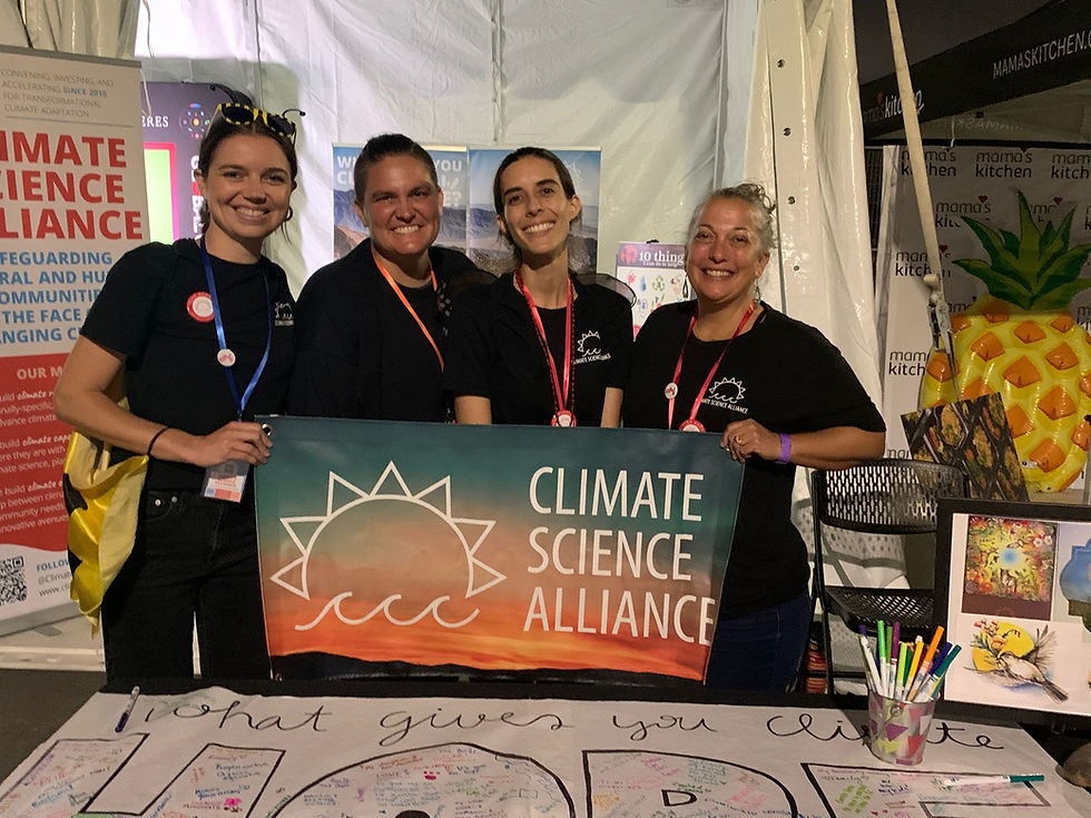 Four members of the Climate Science Alliance team hold up a Climate Science Alliance sign at their booth.