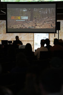 Projection screen of a still from the MAATHAAW extended trailer showing Joelene Tamm working in a forested landscape.