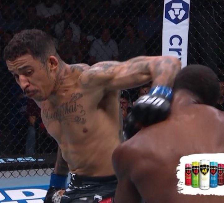 Intense MMA fight scene for Boston Boxing enthusiasts to analyze: Fighter with tattoos throws a punch at opponent inside the cage. Intense action, ad for energy drinks in corner.
