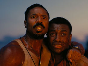 Two men with intense expressions, one holding the other protectively. They are under a dim sky, creating a tense and dramatic mood.