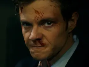 A slightly bloodied man dressed in a smart bank suit gets ready to fight