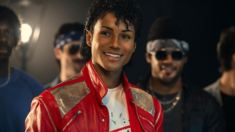 Smiling person in a red jacket with sparkly shoulders stands in front of others wearing dark bandanas. Bright light in the background.