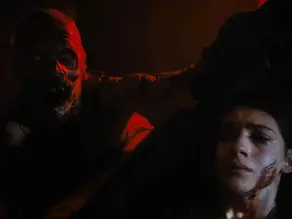 Zombie looms over frightened woman in dark room, lit by red glow. Her face shows fear, with blood on her cheek. Eerie atmosphere.