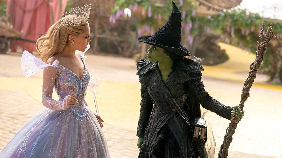 A fairy in a pastel gown and tiara faces a green-skinned witch in black, holding a staff. The yellow brick road and lush scenery form the background.