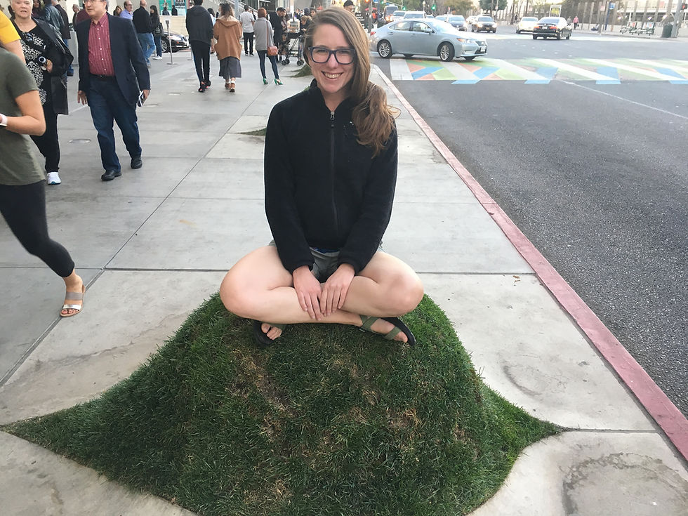 Picture of Carolyn Durham, smiling. She is sitting on top of a decorative grass mound in downtown Los Angeles.