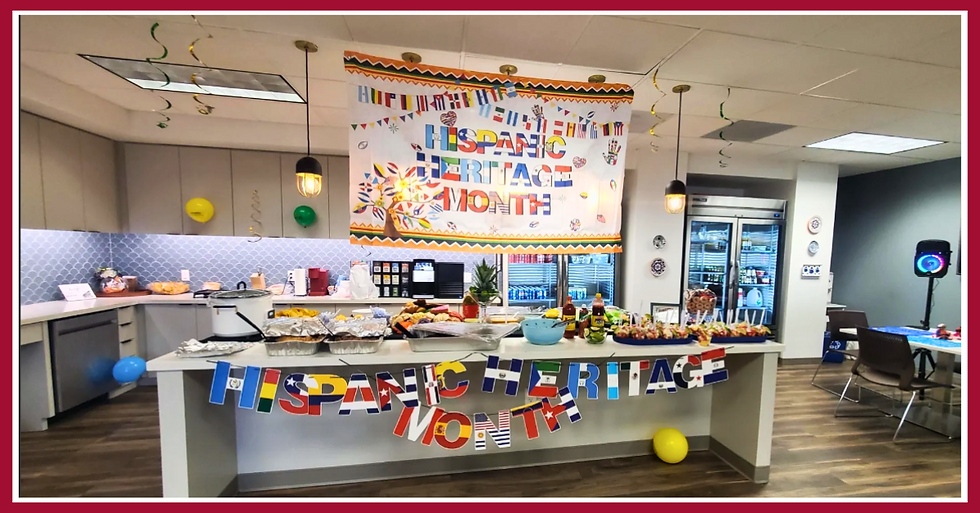 A large office kitchen with a table filled with Hispanic foods. A large colorful banner is hanging from the ceiling to celebrate Hispanic Heritage Month.