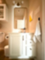 Bathroom with white cabinets, gold-framed mirror, towel, and soap dispenser. Neutral walls and a toilet in a cozy setting.