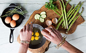 cracking eggs into a bowl with asparagus on the side of a cutting board