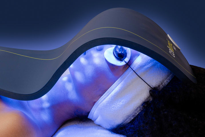 A lifestyle photograph by Brighton lifestyle photographer Stuart Price, showcasing a wellness treatment in Sussex. The image features a woman lying down with a futuristic LED facial mask emitting a blue light. A protective eye cover is placed over her eye. The lighting highlights the advanced technology used in the skincare procedure. The composition captures the serene and professional atmosphere, typical of Stuart Price's lifestyle photography, emphasizing modern skincare and relaxation.