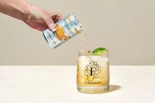 A refreshing Folkington’s Dry Ginger Ale is being poured from a sleek can into a branded glass filled with ice and garnished with a fresh lime wedge. The effervescent drink cascades smoothly, creating a dynamic splash effect. Captured with expert lighting against a neutral beige background, this Sussex drinks photograph by Brighton drinks photographer Stuart Price highlights the crisp, premium quality of the beverage. A perfect composition for showcasing artisan soft drinks, cocktail mixers, and luxury refreshments.