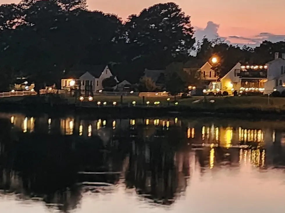 Wide-angle view of home lights reflecting on a calm creek at dusk.