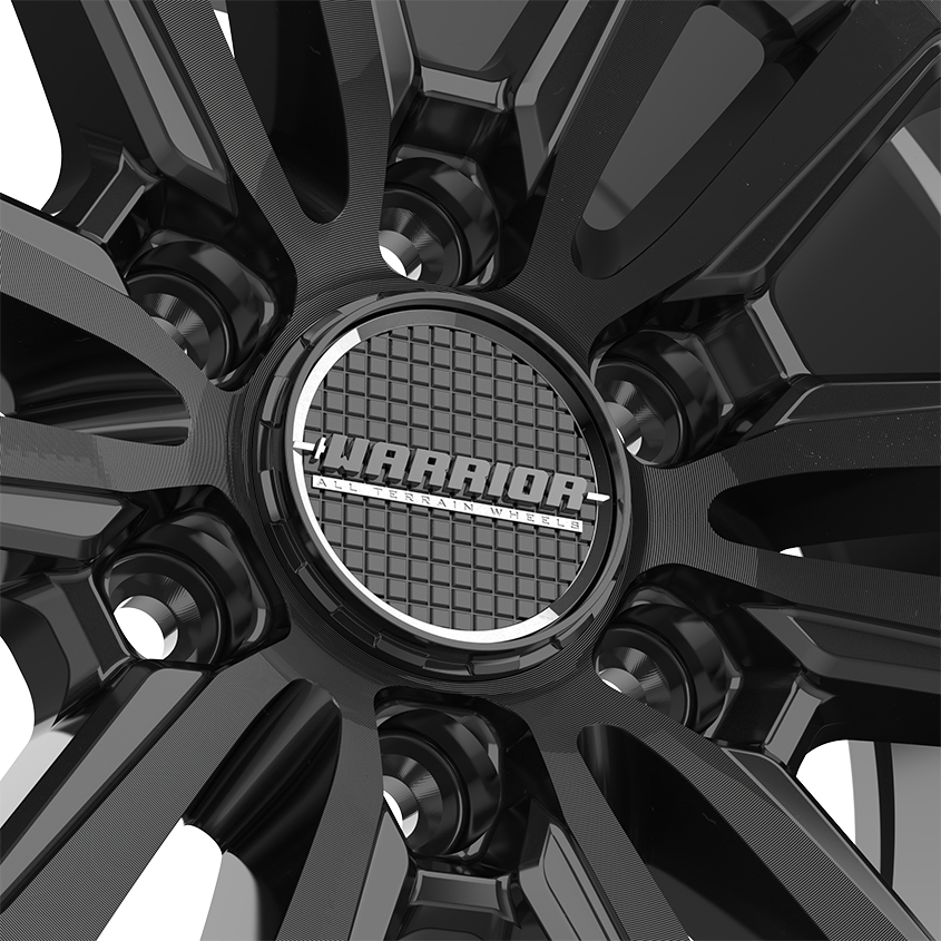 The Warrior wheel cap stands out with its striking gloss black finish and impeccable craftsmanship. The cap’s surface features a finely applied, high-quality paint, showcasing a superior coating process. Surrounding it is a beautifully plated metallic ring, adding an elegant chrome-like touch. Beneath the cap, a distinctive grid pattern reflects the intricate design and attention to detail. This blend of refined aesthetics and sophisticated engineering enhances the wheel’s overall look, offering both style and durability.