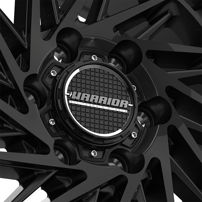 The Warrior wheel cap stands out with its striking gloss black finish and impeccable craftsmanship. The cap’s surface features a finely applied, high-quality paint, showcasing a superior coating process. Surrounding it is a beautifully plated metallic ring, adding an elegant chrome-like touch. Beneath the cap, a distinctive grid pattern reflects the intricate design and attention to detail. This blend of refined aesthetics and sophisticated engineering enhances the wheel’s overall look, offering both style and durability.