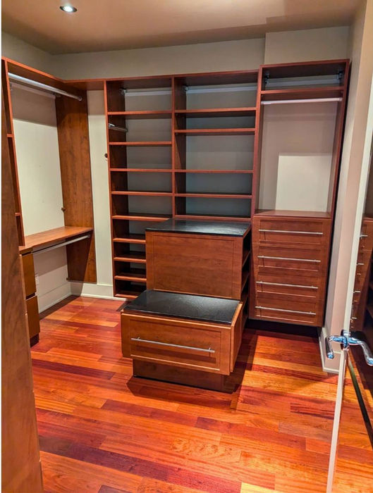 Walk-in closet with freshly painted neutral walls that highlight custom wood shelving and rich hardwood flooring.