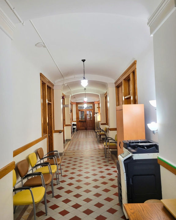 Long hallway with fresh white walls, wood trim, and patterned tile floor in a historic building.