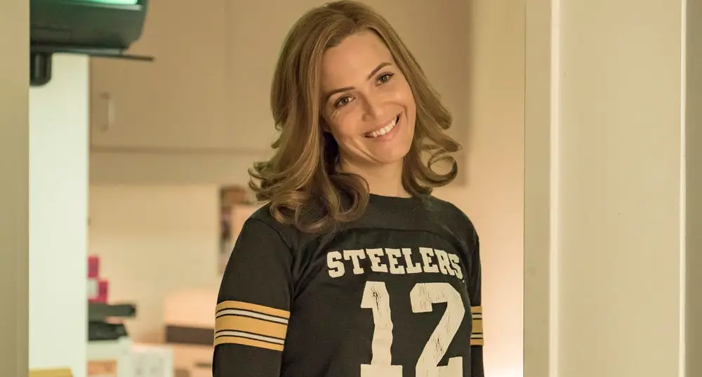 Rebecca Pearson from This is Us standing in a doorway with her head tilted to the side, smiling and wearing a Steelers shirt