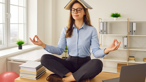 Femme Manager avec lunettes assise en tailleur sur son bureau, position lotus, yeux fermés un livre ouvert sur la tête