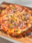 Baked pizza with pepperoni and pineapple on a wooden board.