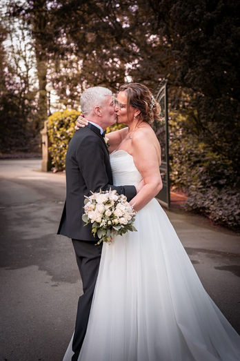 Natural wedding portrait of Lisa and Carl kissing on the driveway at Bartle Hall, Lancashire