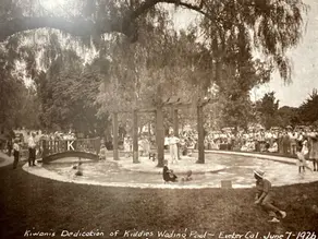 Crowd gathers for a wading pool dedication in Exeter, CA, June 7, 1926. Children play in water; bridge with "K" visible.