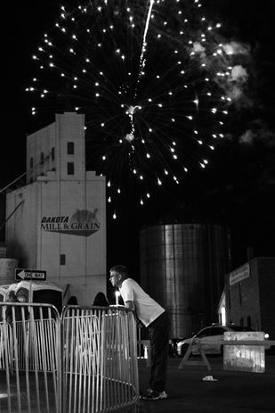 Black and white photography of fireworks over a grain silo at a small-town carnival by Little Rock artist Katie Adkins. 