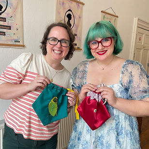 Two women smiling as they hold up the reticules they have made as part of a creative workshop inspired by Jane Austen in Bath