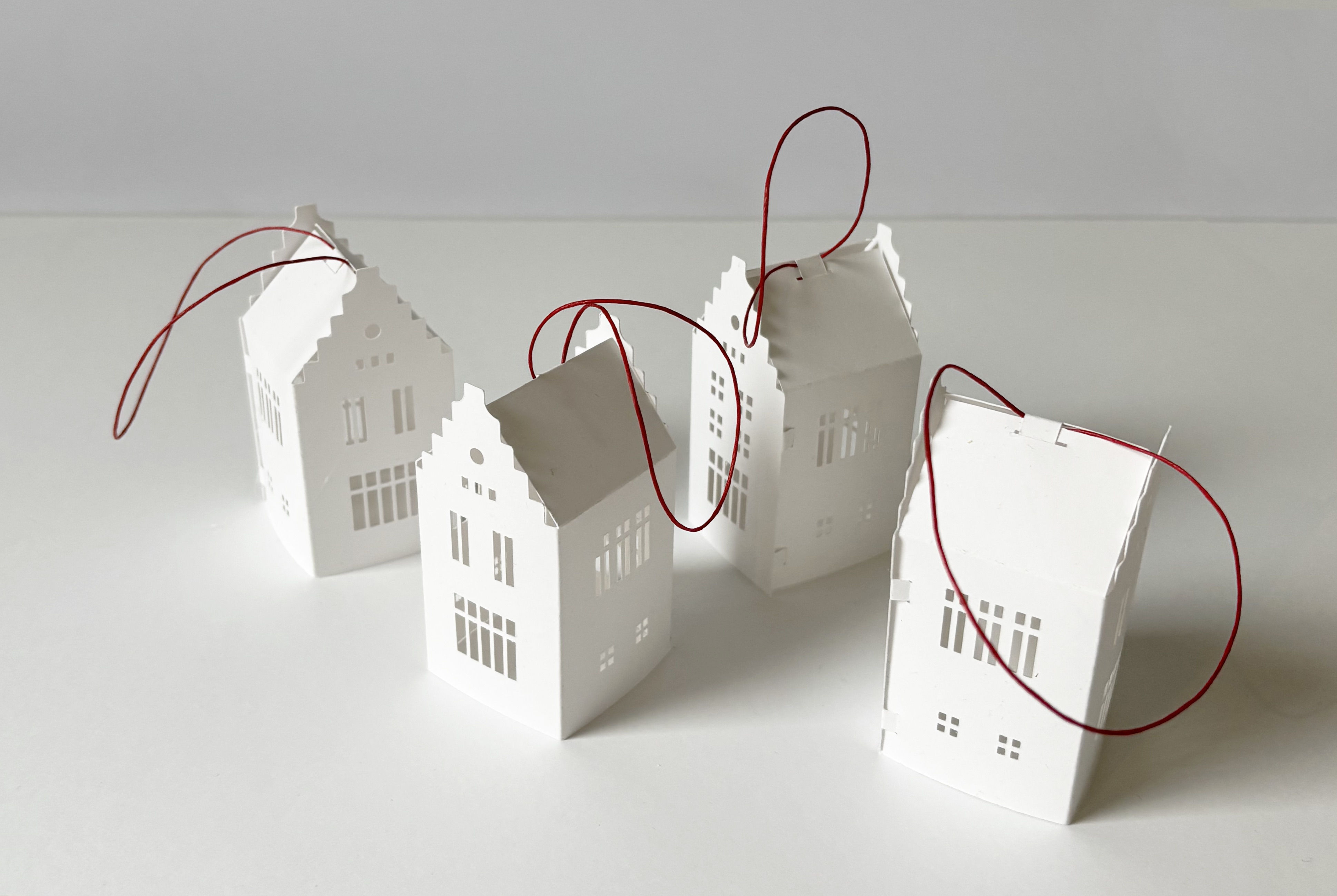 Four white small paper house ornaments with hanging stripe
