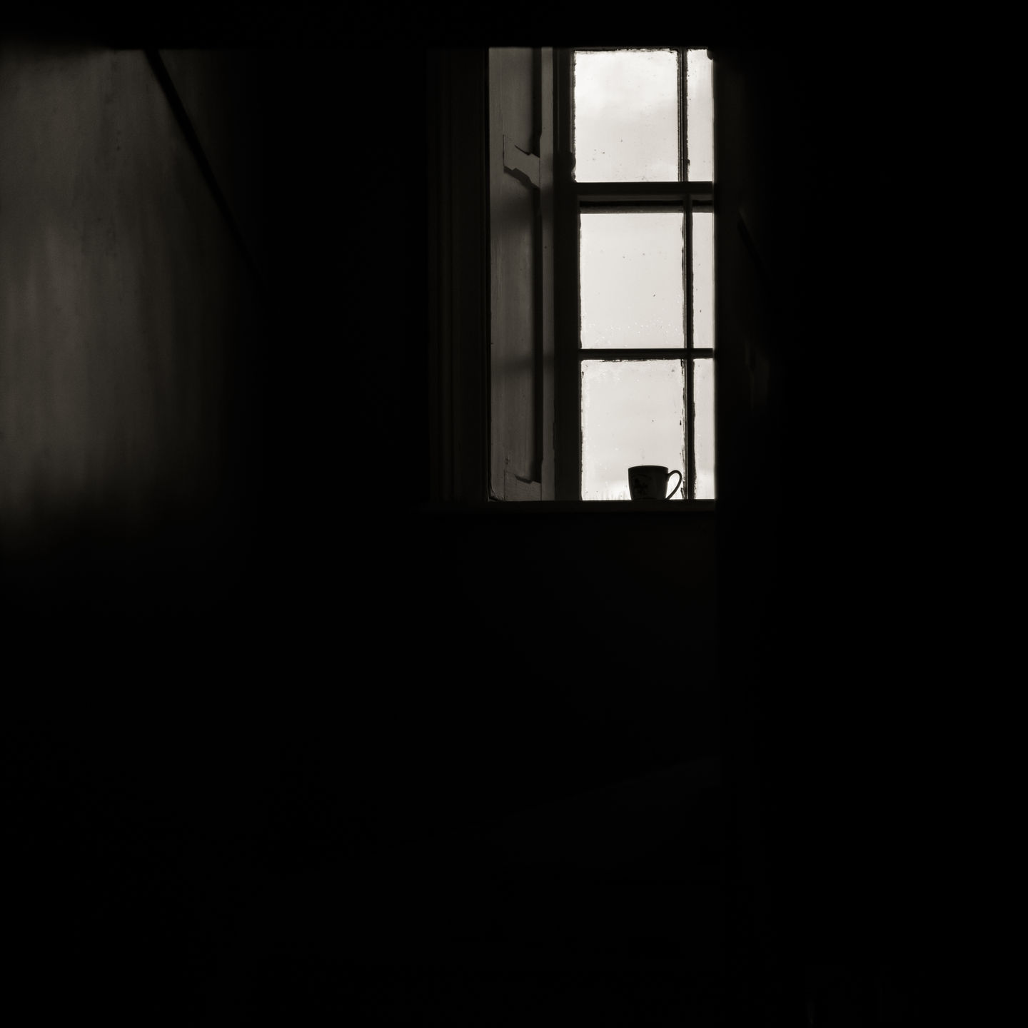 a black and white photo of a window with a cup on the sill
