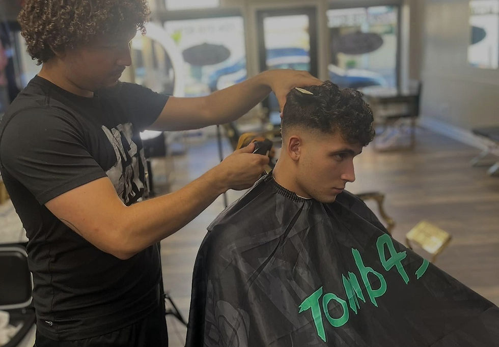 CDougFadez barber cutting hair in his shop. He is giving a mid taper fade to the young man in the chair
