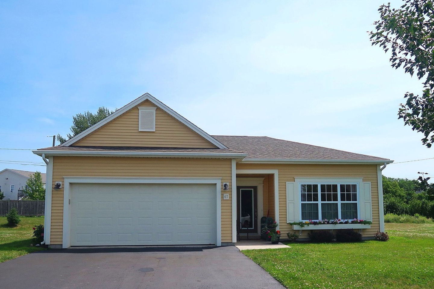 Yellow ranch style house with a garage door and a window box