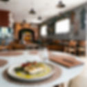 Prato de peixe com aspargos e tomates em mesa de restaurante; ao fundo, salão vazio com decoração em tons neutros.