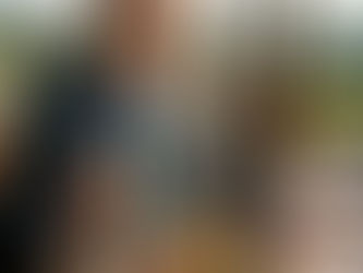 Homem de terno come prato de frutos do mar em restaurante ao ar livre, com taça de vinho e vinhedos ao fundo.